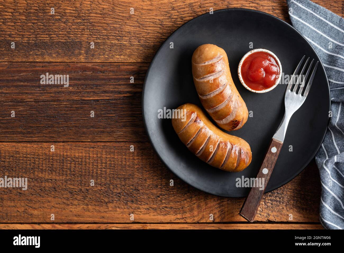 Saucisses grillées avec sauce tomate sur une assiette sur fond de table en bois, vue du dessus de l'espace de copie Banque D'Images