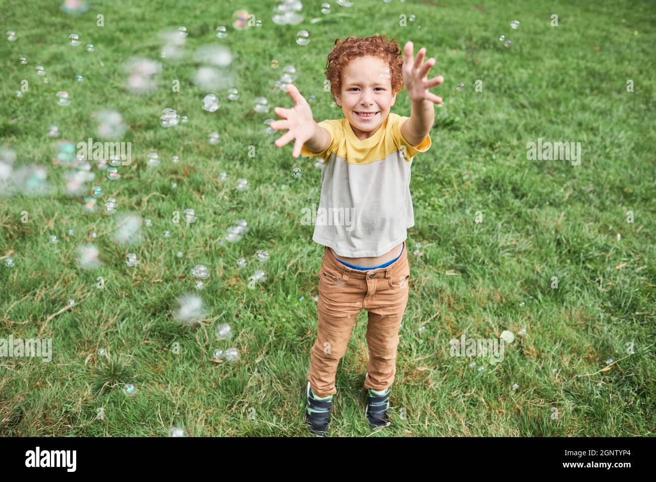 Portrait complet d'un adorable garçon souriant jouant avec des bulles tout en appréciant la fête d'anniversaire à l'extérieur en été Banque D'Images