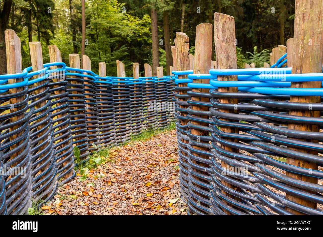 Chemin d'automne avec feuilles tombées entre une clôture faite de tuyaux en plastique tordus en noir et bleu tressé entre les poteaux en bois. Utilisation alternative de tuyaux de plomberie en polypropylène dans la conception de paysage. Banque D'Images
