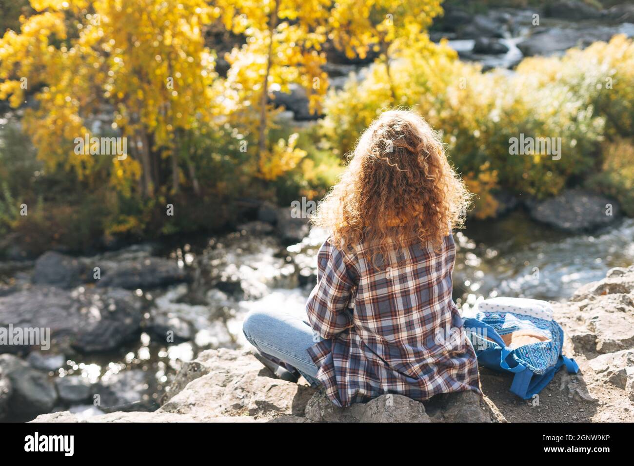 Jeune belle femme avec des cheveux bouclés dans un maillot à carreaux, jeans regarde la vue magique des montagnes et de la rivière, randonnée sur la nature automnale, les gens de derrière Banque D'Images