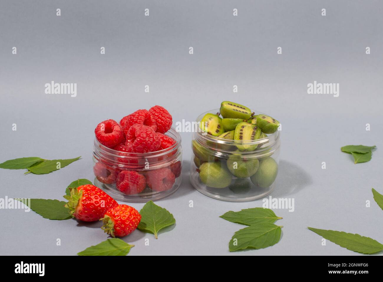 Fruit d'actinidia arguta, fruits aux baies de kiwi, framboises, fraises et feuilles de menthe, sur fond bleu. Banque D'Images