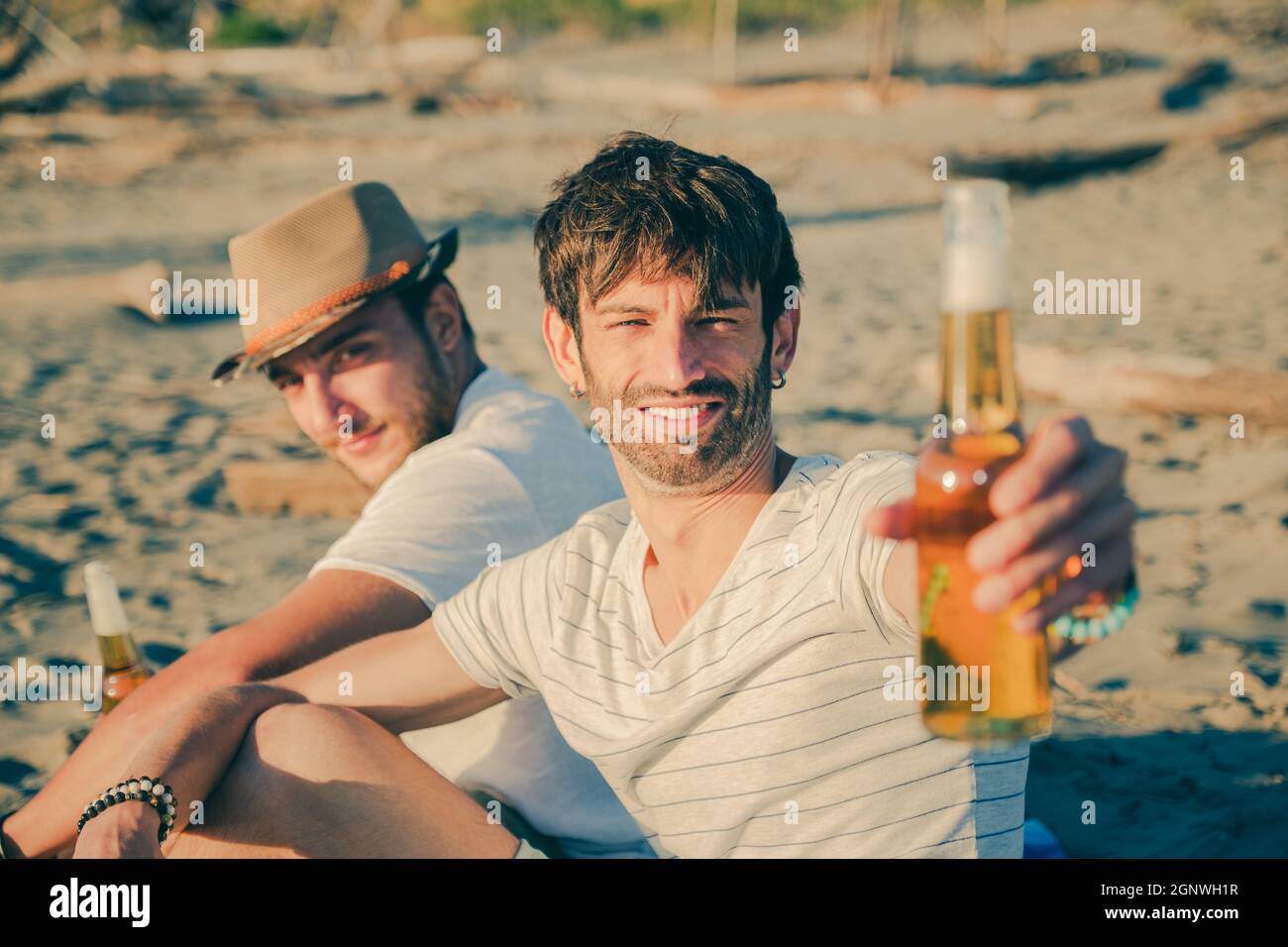 Portrait d'amis se reposer sur la plage en buvant de la bière. Des jeunes gais passent du bon temps ensemble tout en étant assis sur la plage et souriant Banque D'Images