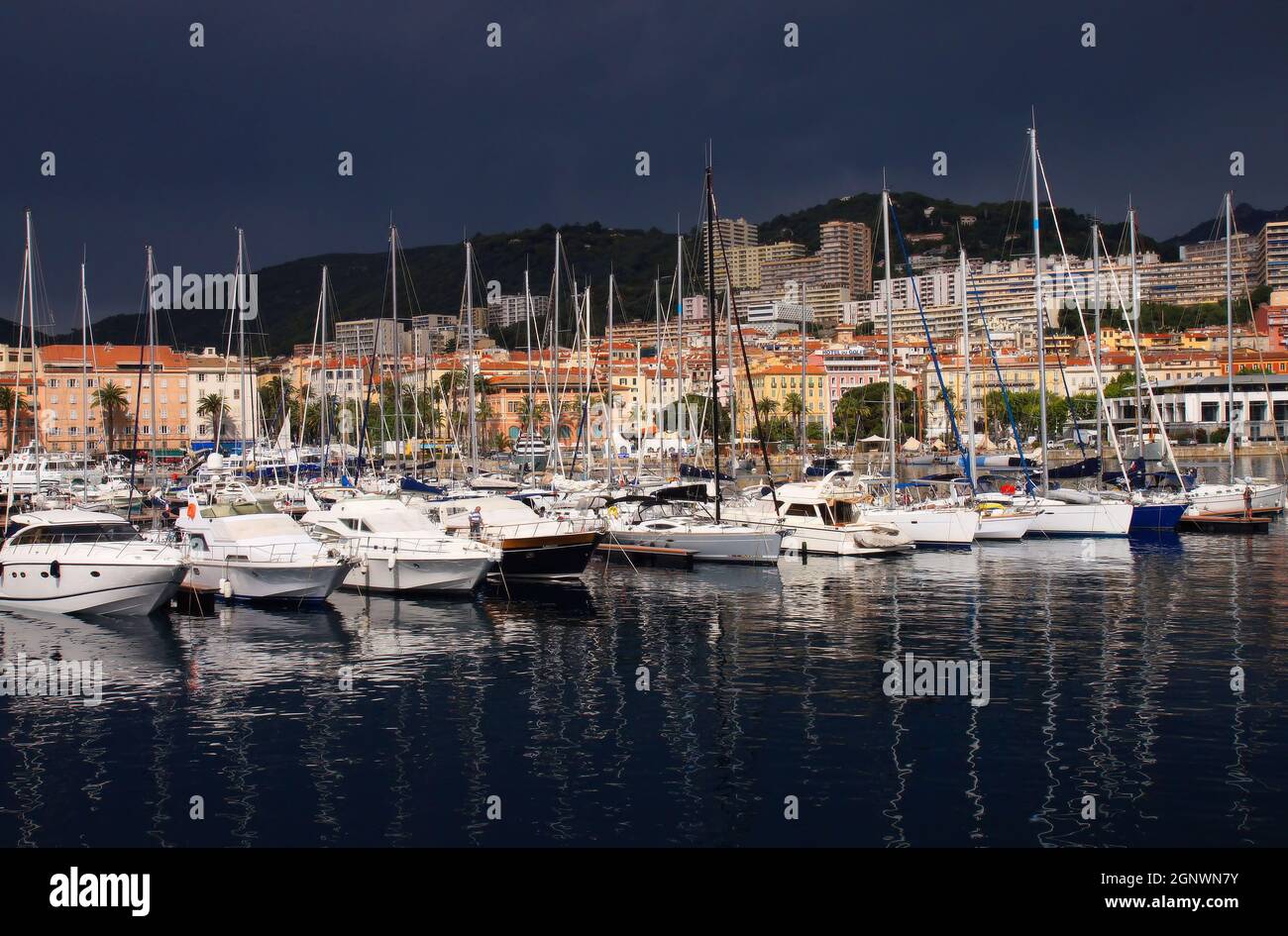 Port, bateaux, bâtiments colorés de la ville et collines avec des nuages noirs sombres juste avant une tempête à Ajaccio, Corse, France Banque D'Images