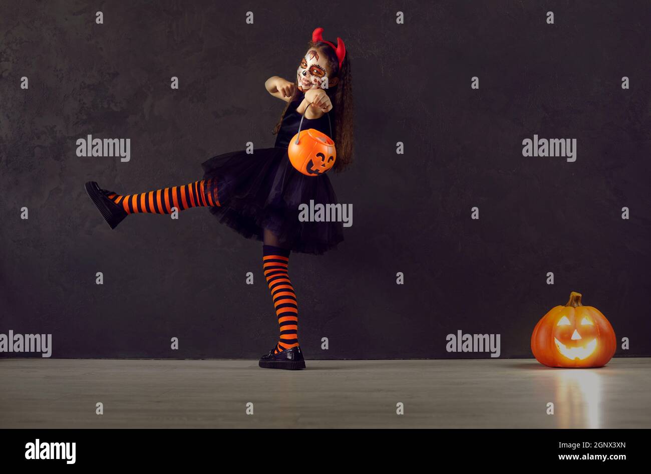 Petite fille en costume d'Halloween avec des marches de seau de bonbons de citrouille sur fond noir. Banque D'Images