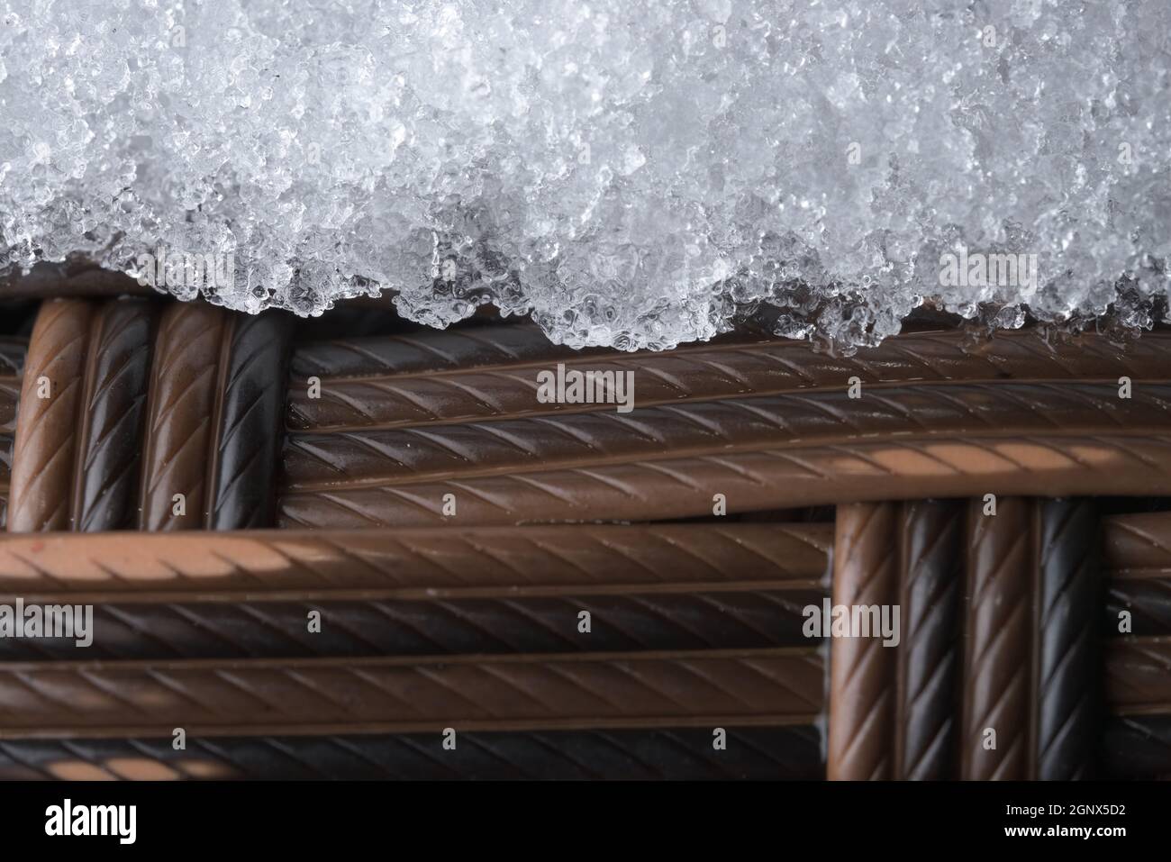 Mobilier de jardin en plastique glacé. Tissu tissé en rotin, mais synthétique. Le temps froid en extérieur a provoqué la formation d'une couche de neige ou de givre. Banque D'Images