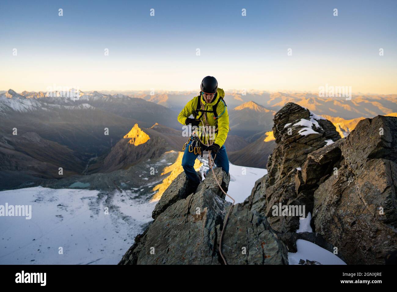 Homme alpiniste escalade de formation naturelle de roche et essayant d'atteindre le sommet de montagne. Au coucher ou au lever du soleil. Grimpeur de roche avec veste jaune. Concept o Banque D'Images