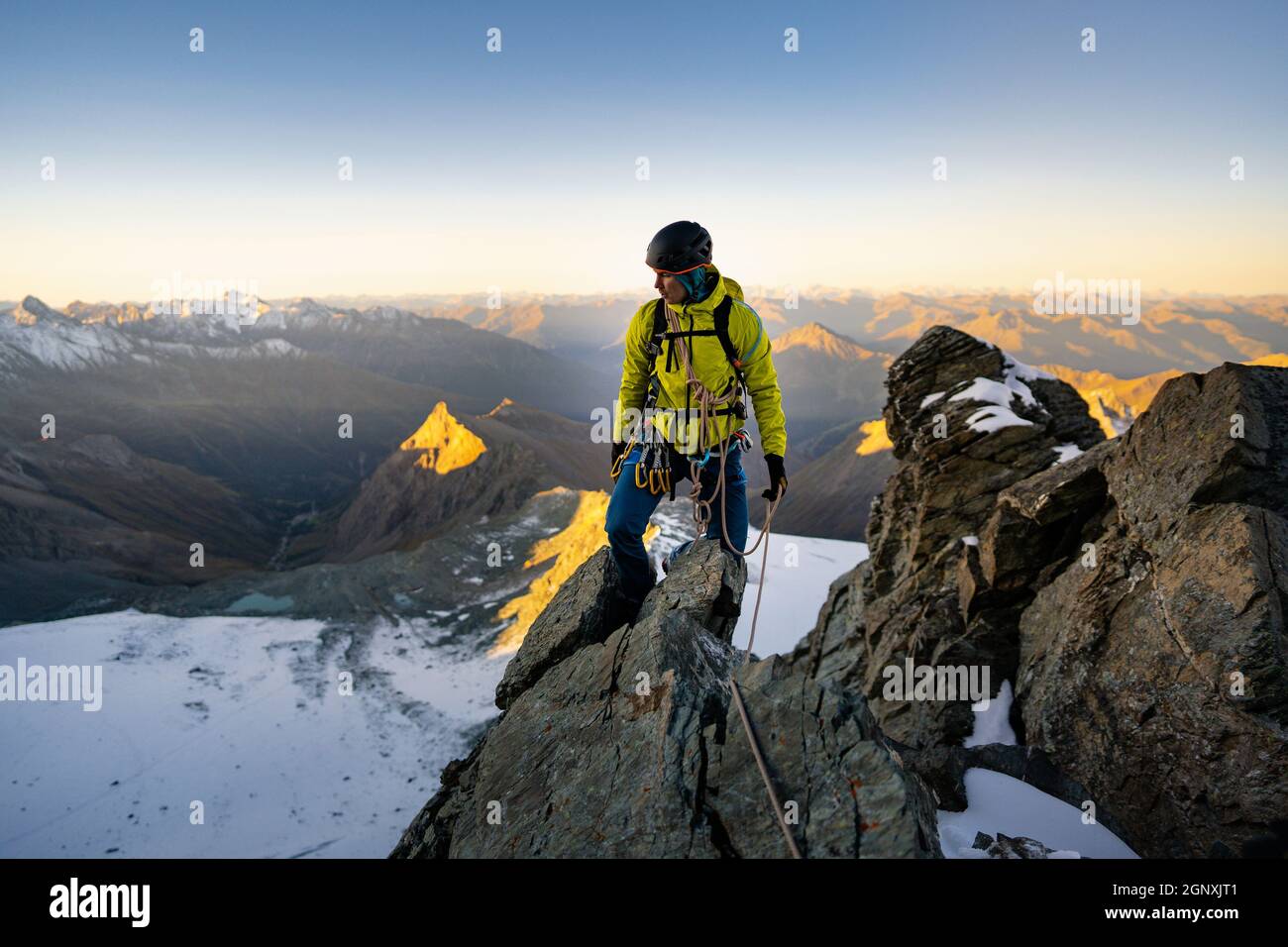 Homme alpiniste escalade de formation naturelle de roche et essayant d'atteindre le sommet de montagne. Au coucher ou au lever du soleil. Grimpeur de roche avec veste jaune. Concept o Banque D'Images