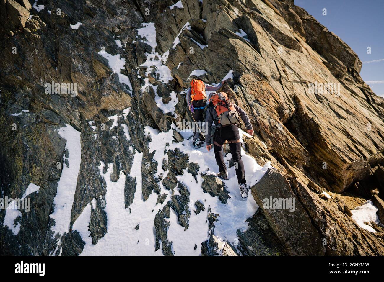 Vue arrière des grimpeurs avec sacs à dos à l'aide d'une corde fixe tout en montant haute montagne rocheuse. Hommes alpinistes escalade formation naturelle de roche Banque D'Images
