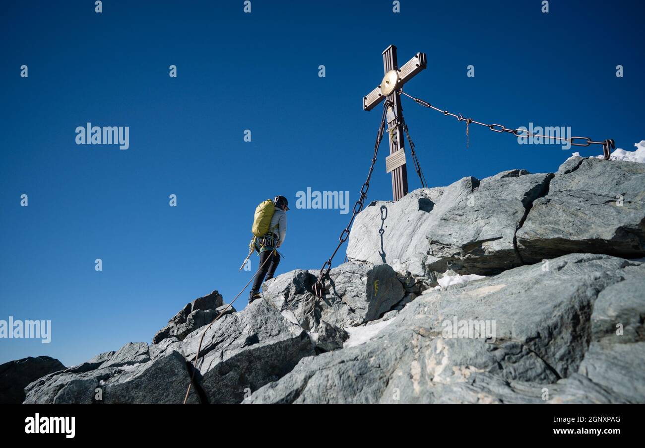 Une femme en tenue de randonnée atteignant la croix sur Grossglockner, la plus haute montagne d'Autriche. Effacer le jour. Réalisation. Fille sur le sommet de la crête Banque D'Images