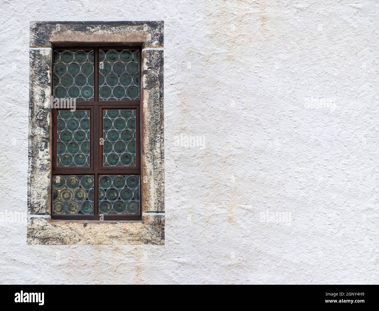 ancienne fenêtre en verre au plomb avec encadrement en pierre et un mur de maison en plâtré clair et texturé avec espace de copie à droite Banque D'Images