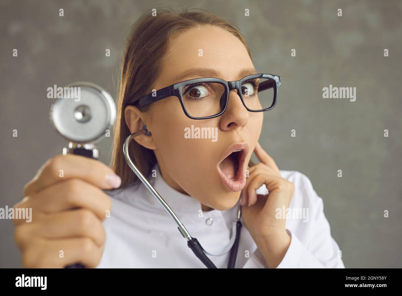 Un médecin de femme choqué avec un visage surpris soulève un stéthoscope à l'écoute du battement de coeur. Banque D'Images