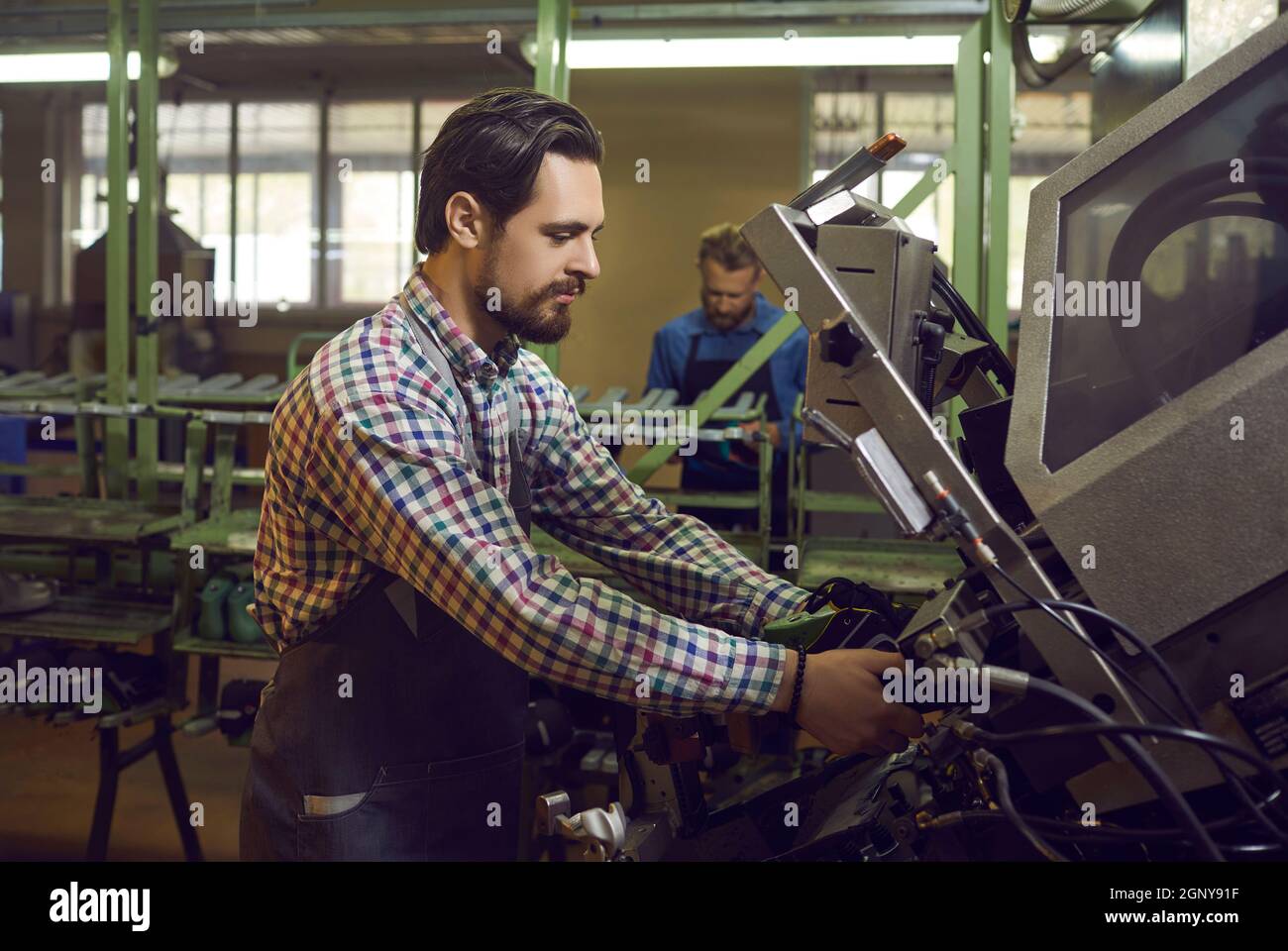 Jeune travailleur utilisant une presse industrielle spéciale tout en faisant de nouvelles chaussures à l'usine de chaussures Banque D'Images