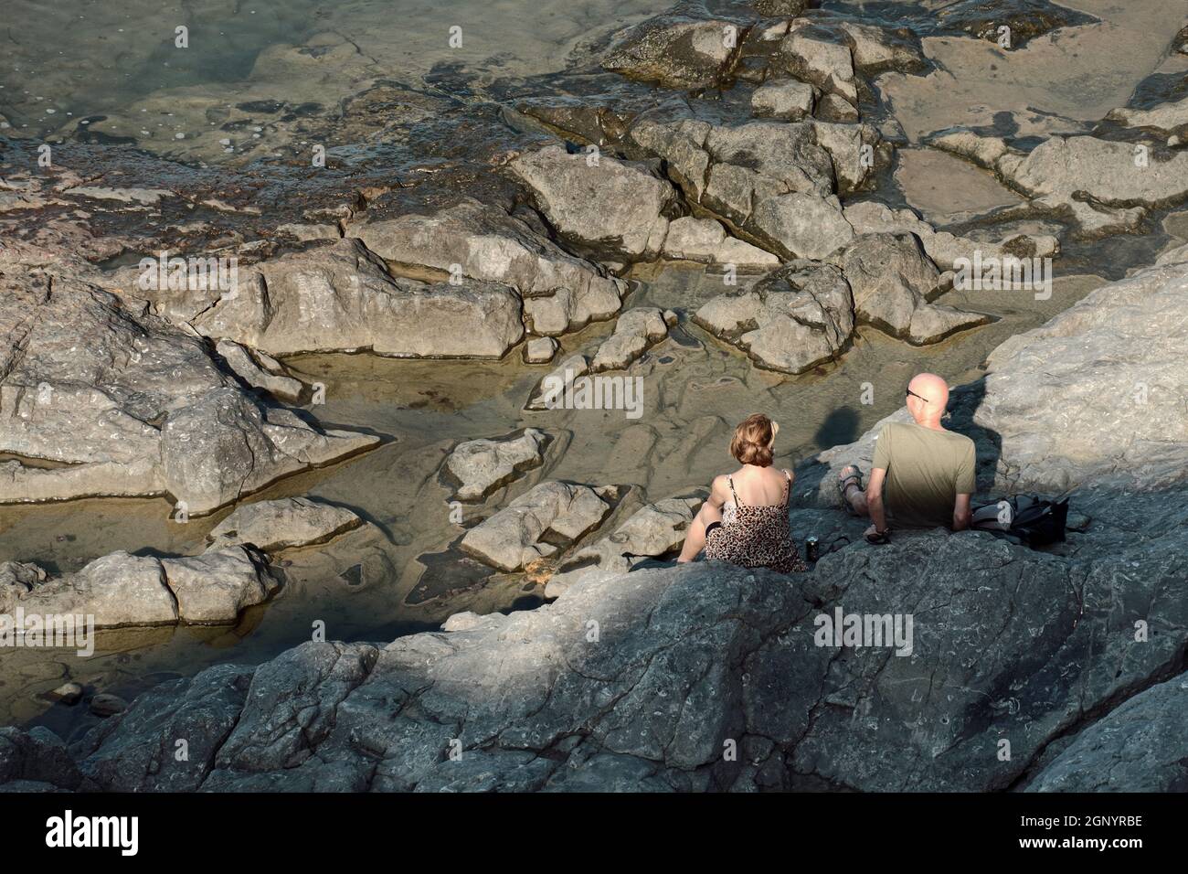 côte rocheuse de Sicile couple de touristes assis sur les rochers de lave au bord de la mer à Cefalù Banque D'Images