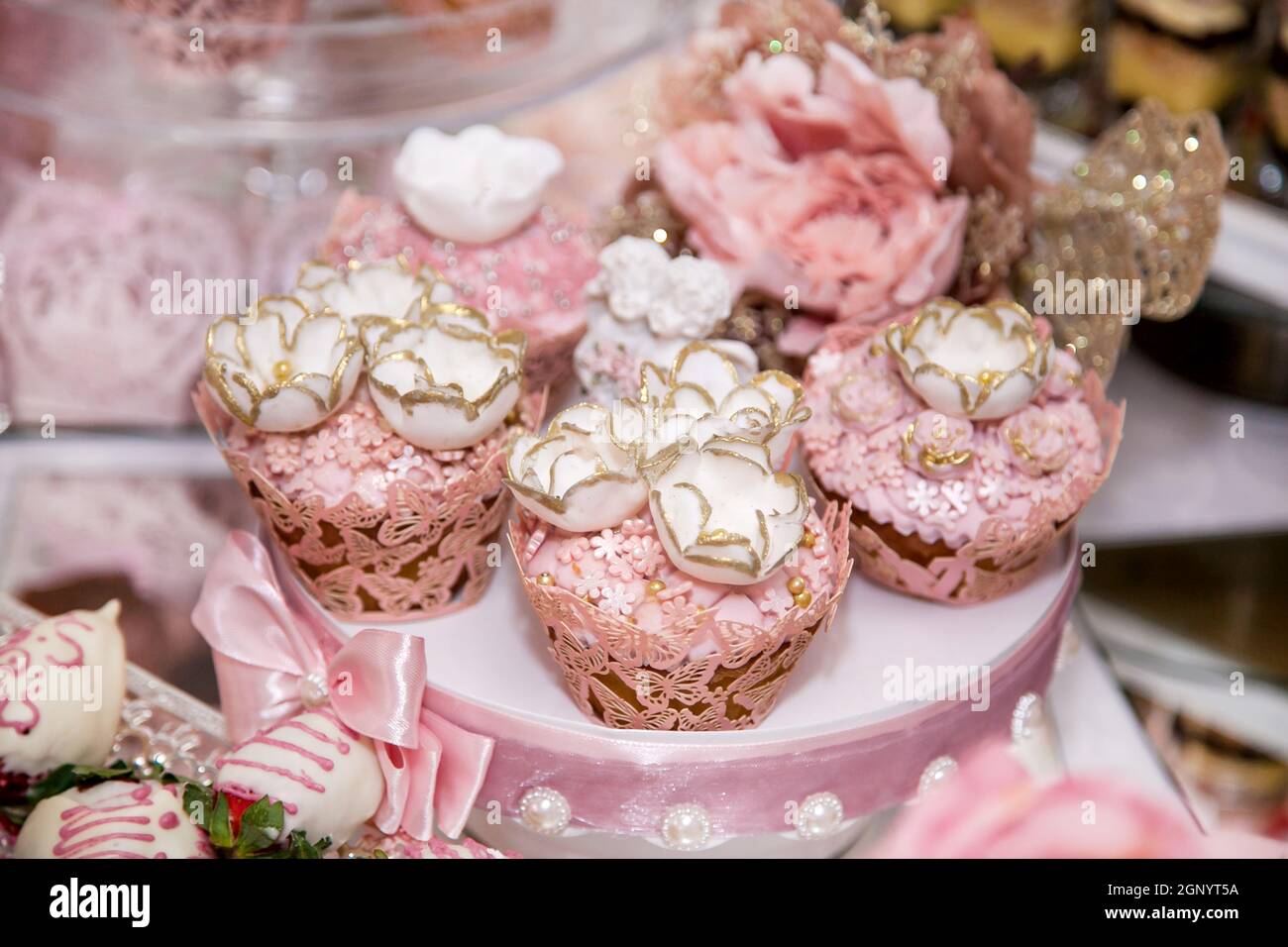 Délicieux desserts au bar à bonbons de mariage dans la zone du buffet : muffins décorés d'anges, rosebuds à sucre et colorant or. Banque D'Images