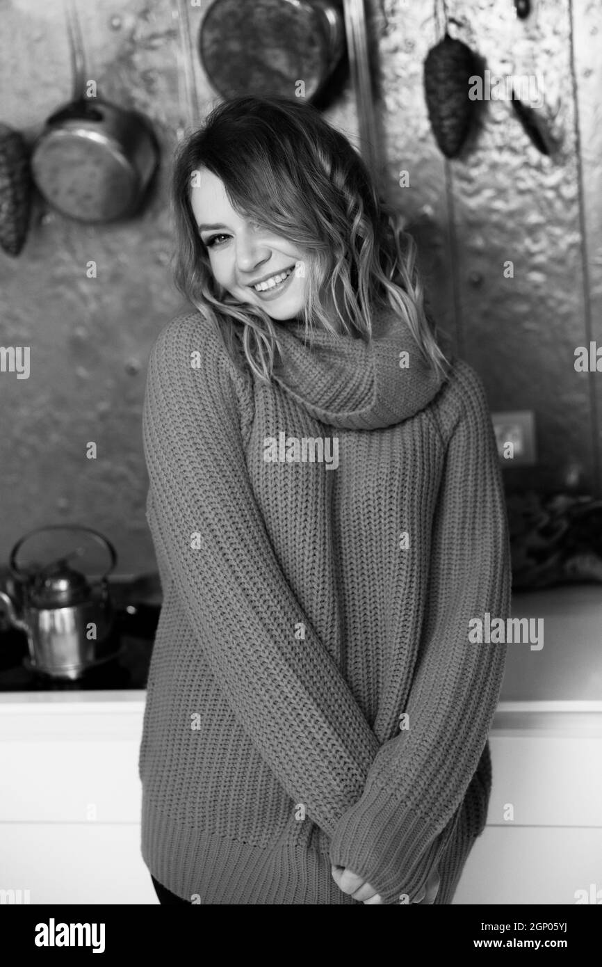 Portrait noir et blanc d'une belle femme souriante dans un pull confortable à la maison. Jeune femme adulte élégante debout dans la cuisine, regardant l'appareil photo Banque D'Images