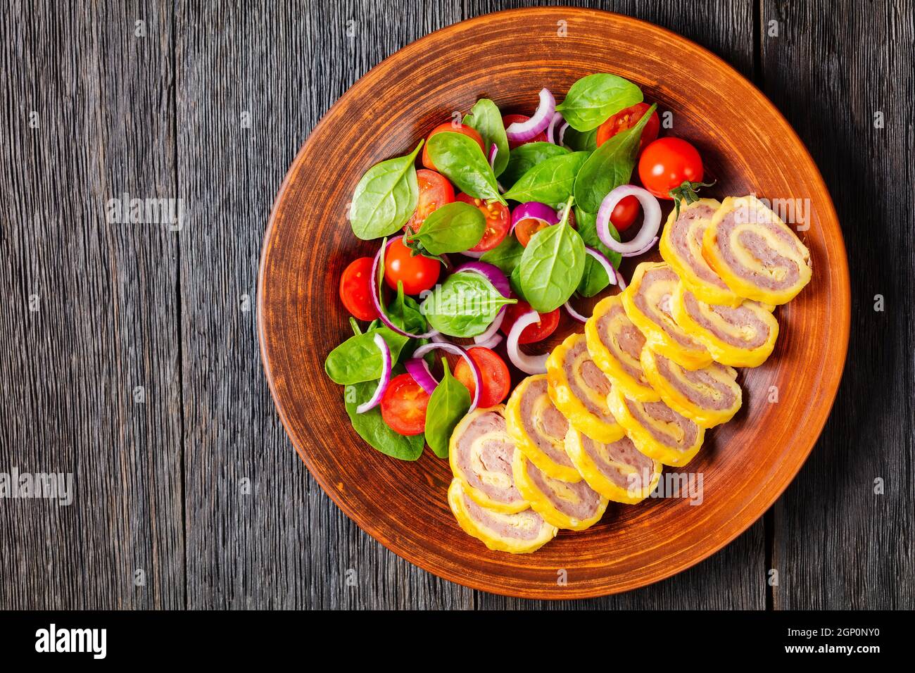 petit déjeuner au jambon et au fromage hachés petits roulés avec salade d'oignons rouges aux épinards frais sur une assiette rustique sur une table en bois, vue horizontale de Banque D'Images