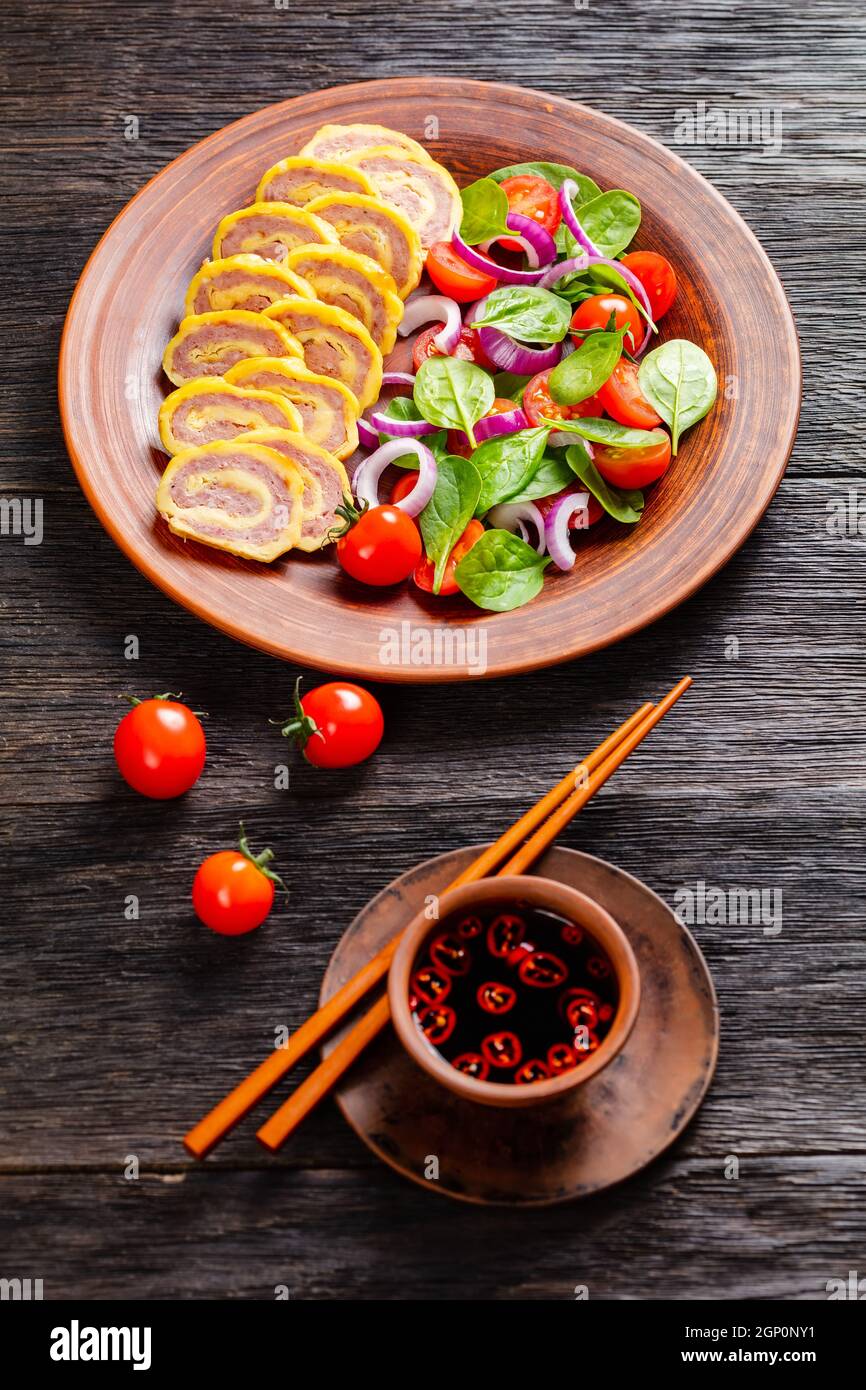 petit-déjeuner au jambon et au fromage, omelettes, pignons d'œufs et salade d'oignons rouges aux tomates épinards sur une assiette rustique sur une table en bois, vue verticale depuis un Banque D'Images