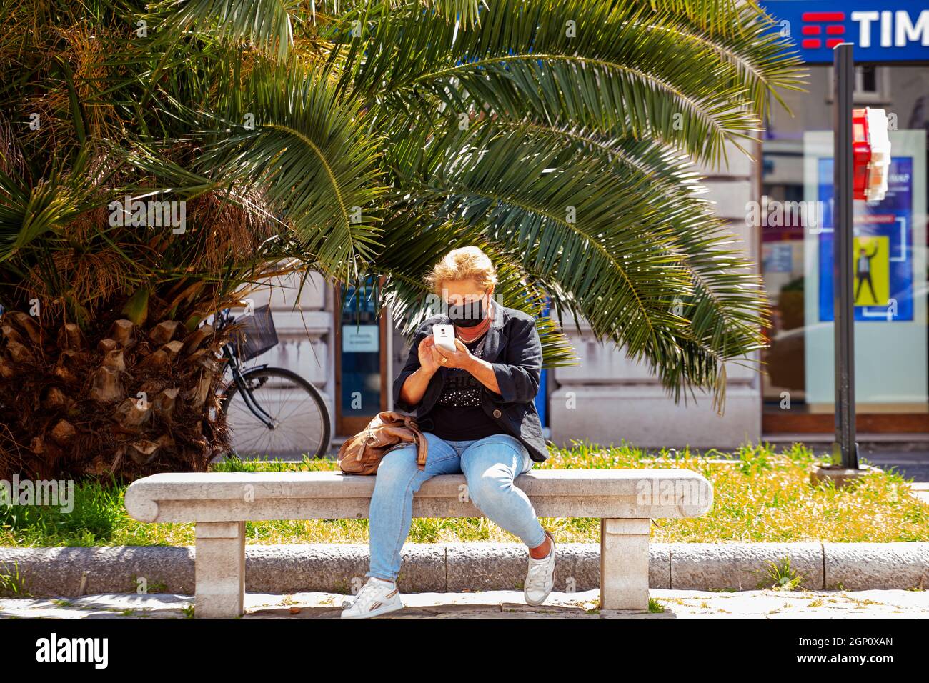 Trieste, Italie - Mai, 31: Vue de la femme senior dans le masque de protection du visage utilise smartphone, navigue sur Internet tout en étant assis sur le banc à l'extérieur le 31 mai Banque D'Images