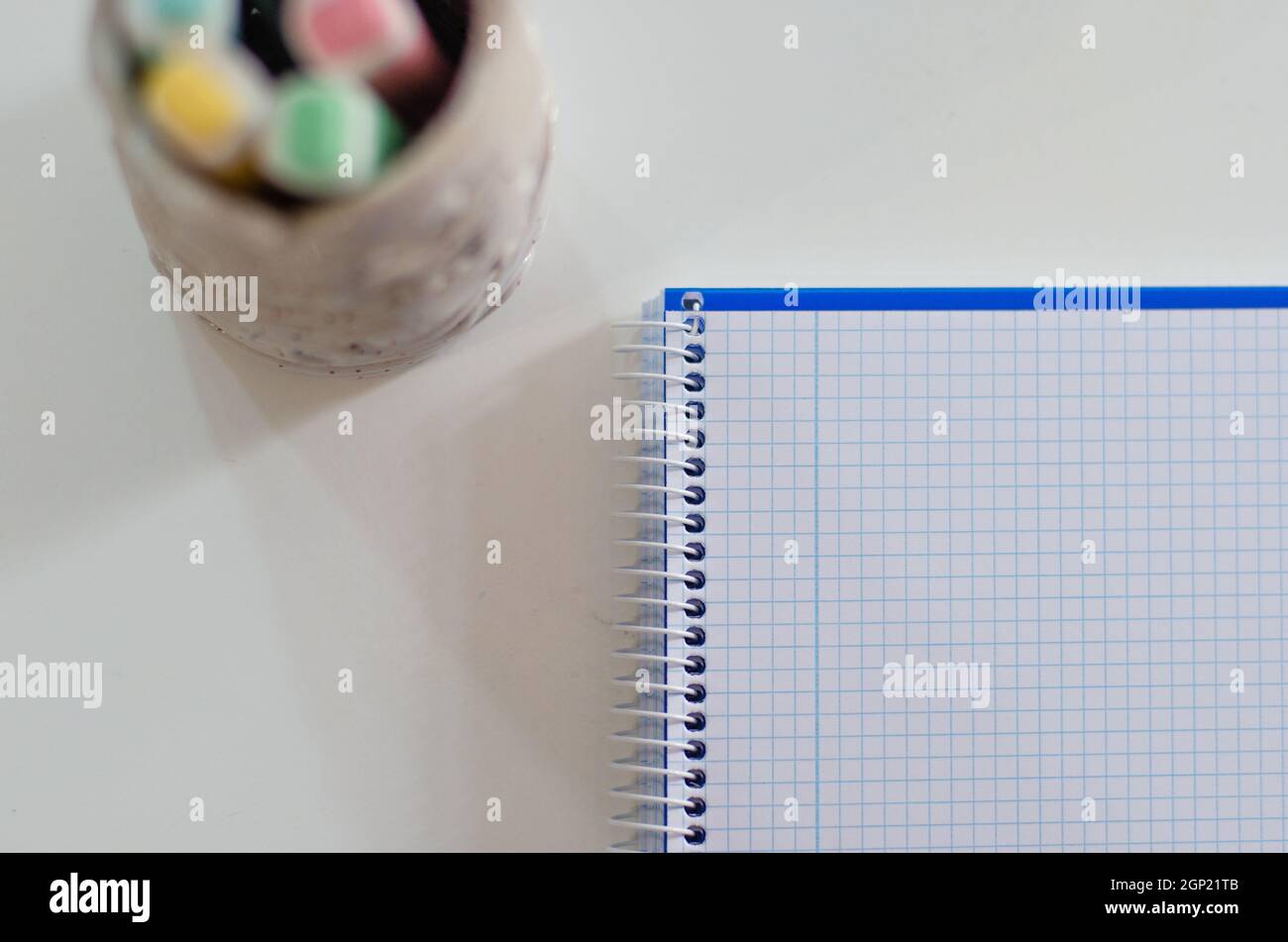 Plusieurs crayons de couleur dans un morceau de céramique sont placés sur une table en bois et un carnet blanc. Concept de retour à l'école Banque D'Images