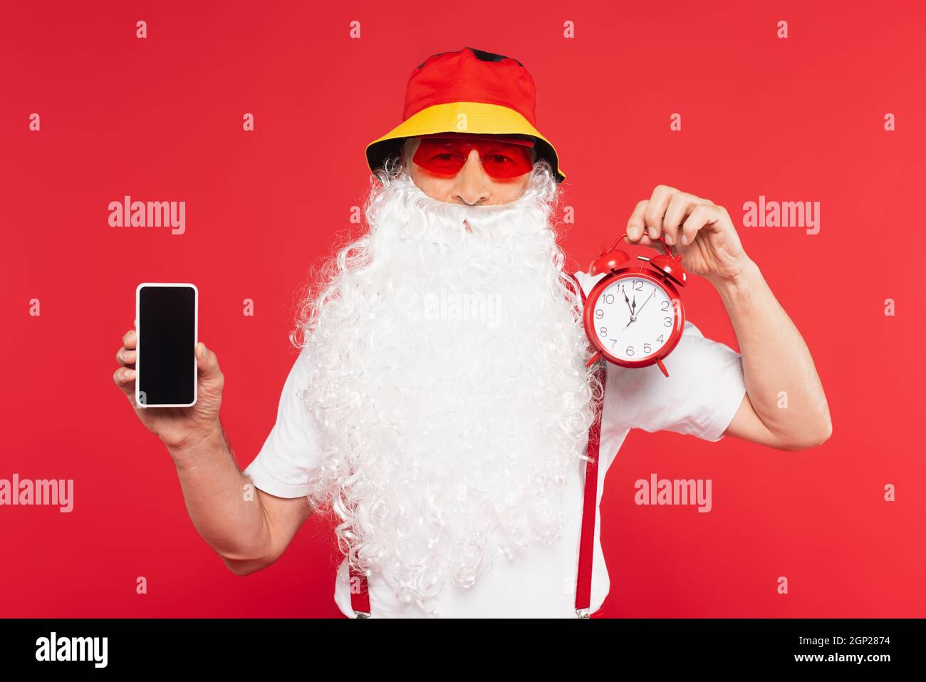 Le Père noël dans des lunettes de soleil tenant un réveil et un smartphone isolé sur le rouge Banque D'Images