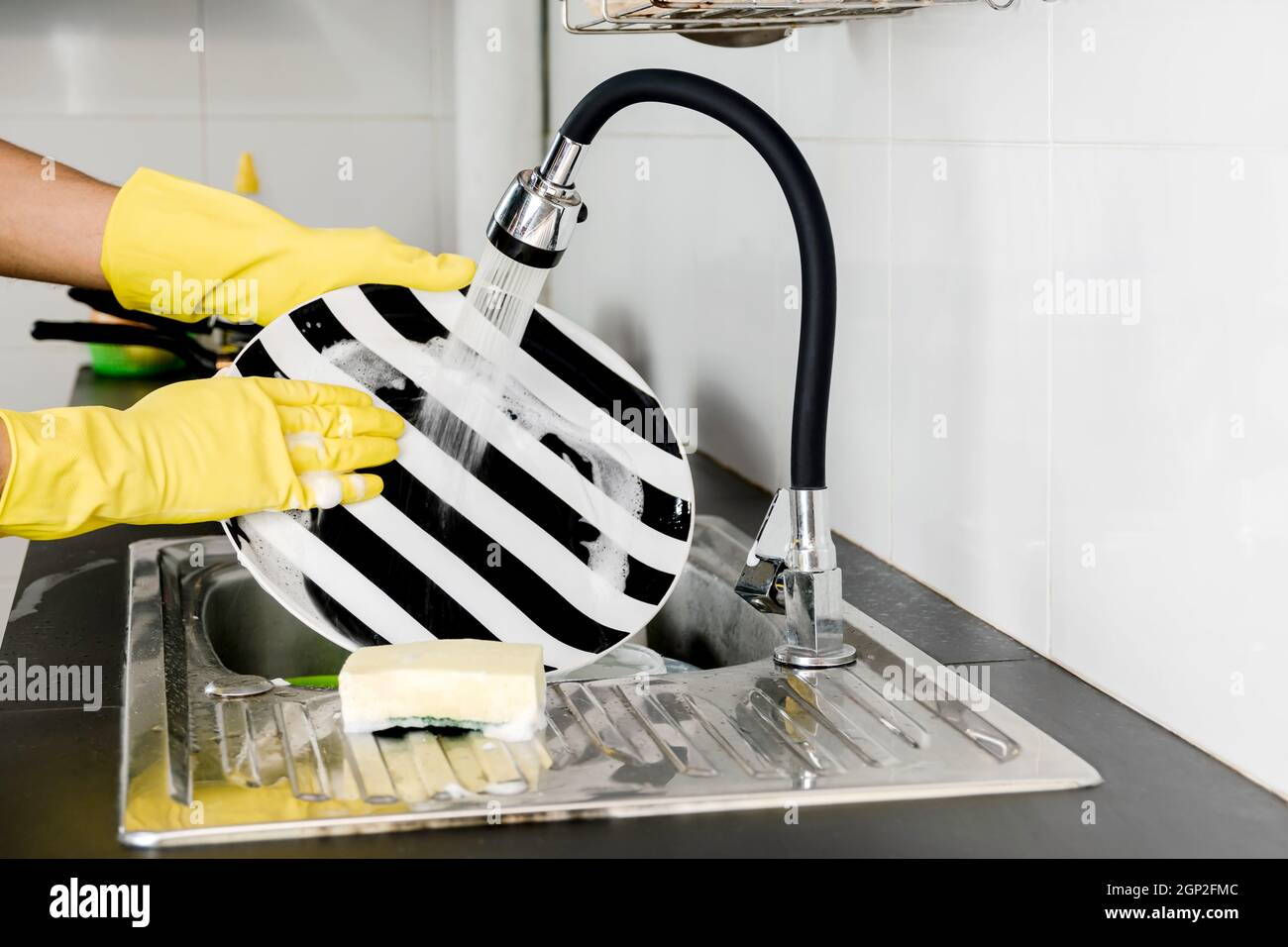 Fermez les mains humaines dans des gants en caoutchouc jaune pour laver la vaisselle dans l'évier de cuisine. Banque D'Images Fermez les mains humaines dans des gants en caoutchouc jaune pour laver la vaisselle dans l'évier de cuisine. Banque D'Images