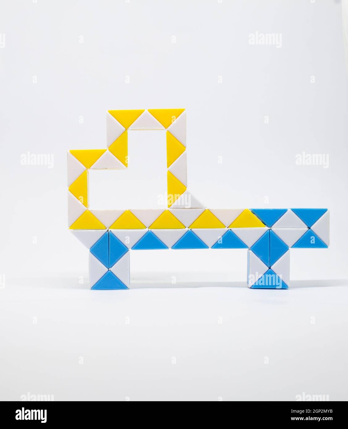 Jouet de camion fait de triangles bleus, jaunes et blancs sur fond blanc. Banque D'Images