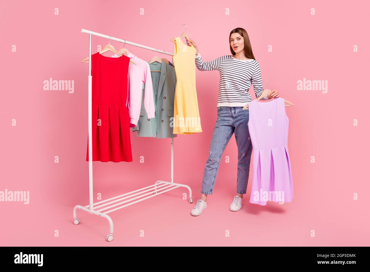Vue sur toute la longueur de corps de fille gaie attrayante choisir une nouvelle robe look isolé sur fond rose pastel couleur Banque D'Images
