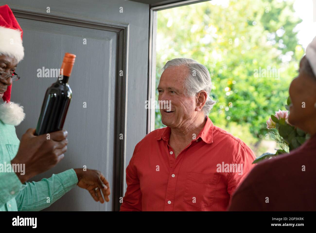 Joyeux homme âgé caucasien avec du vin venant rendre visite à divers amis à l'heure de noël Banque D'Images