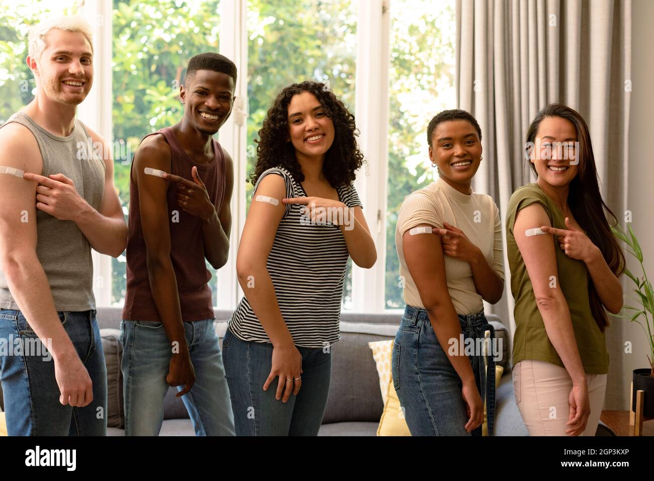 Groupe d'amis féminins et masculins variés heureux montrant des pansements après la vaccination Banque D'Images