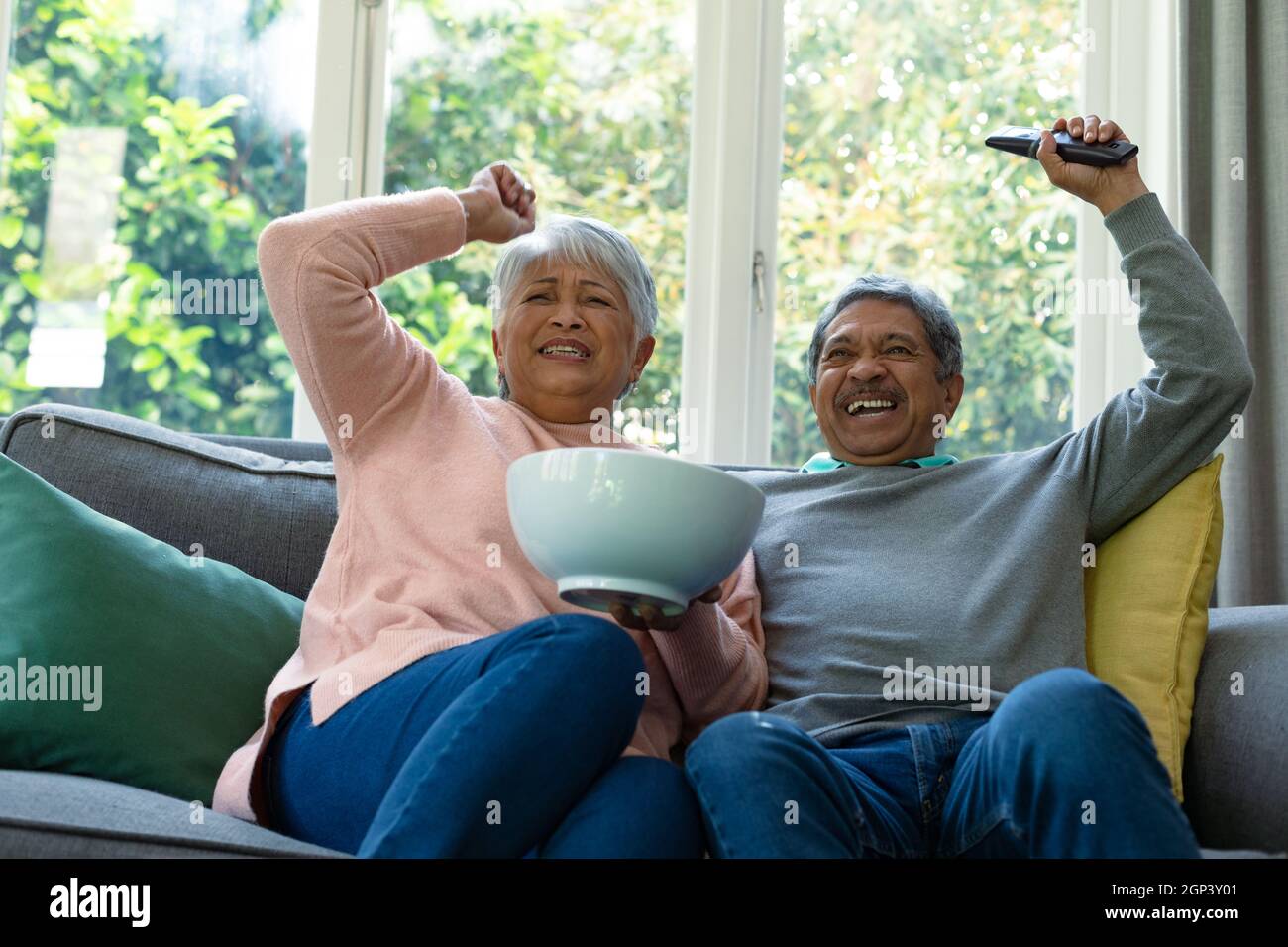 Deux couples âgés divers assis sur un canapé, regardant la télévision et s'amuser Banque D'Images