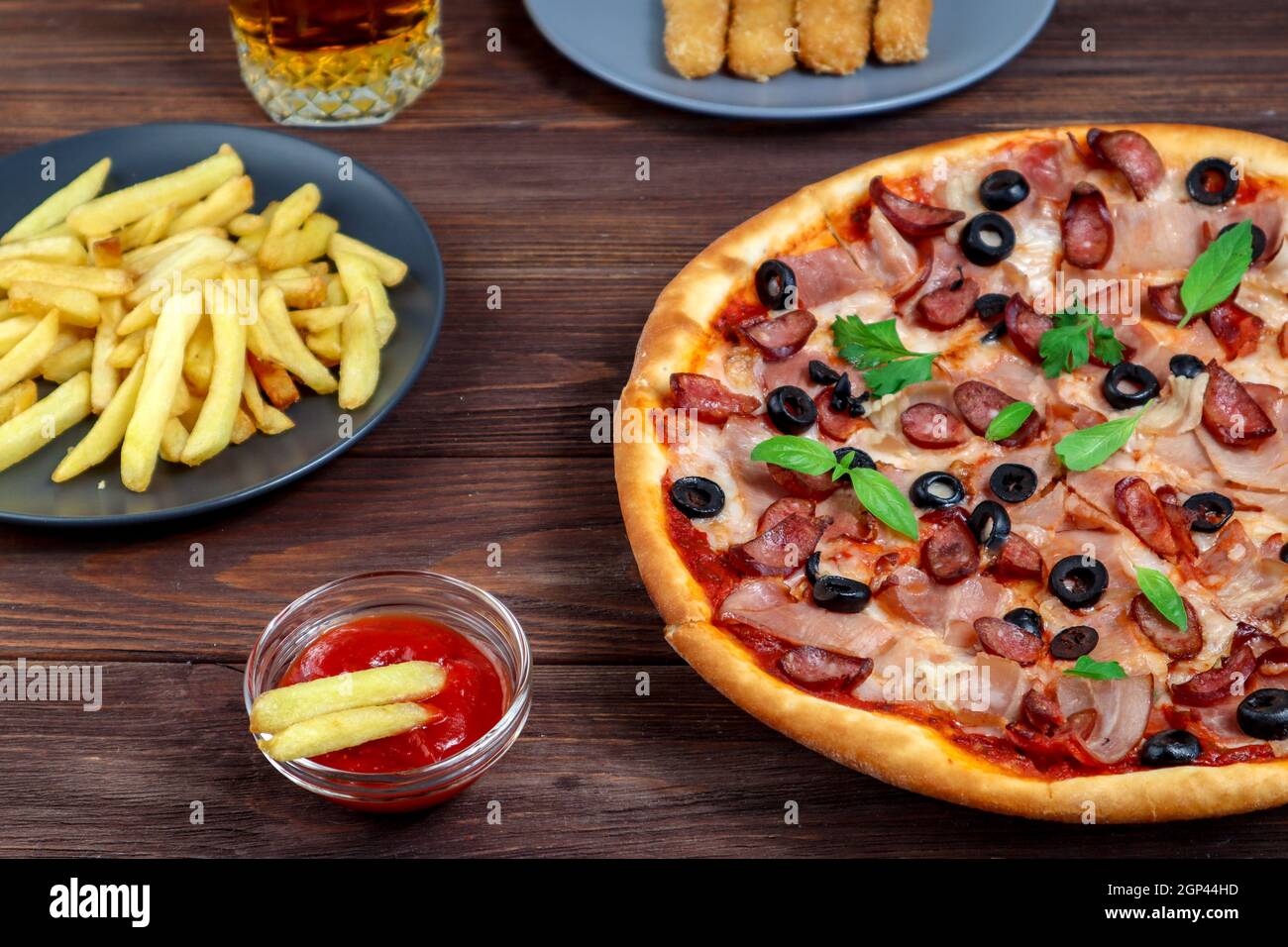 Pizza sur un plateau gros plan sur la table avec ketchup, jus, sauce et pommes de terre sur une table en bois sombre dans le style rustique. Banque D'Images