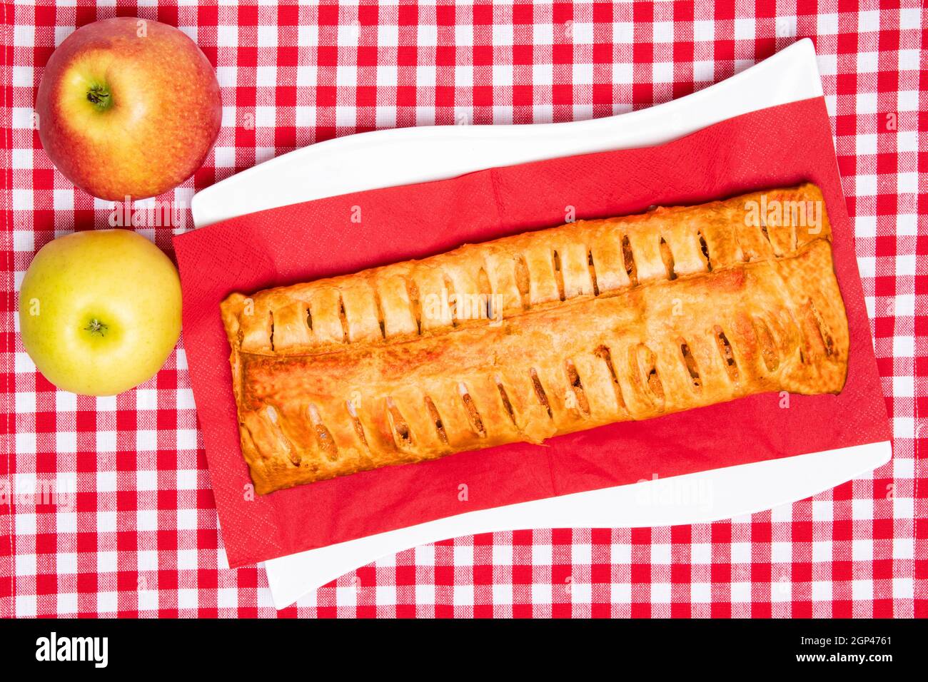 Rouleau de pommes servi. Vue de dessus d'une strudel de pomme fraîche cuite maison avec deux pommes fraîches sur une serviette de pique-nique ou une serviette de table rouge. Gâteau et pâtisserie. SPAC Banque D'Images