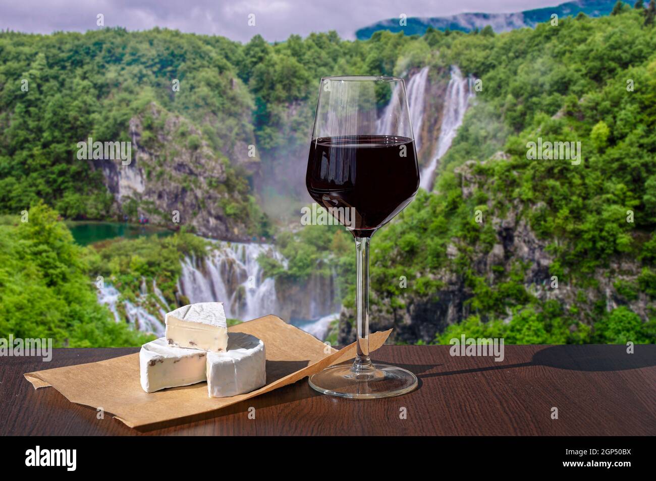 Verre de vin rouge avec en-cas au fromage contre de belles grandes cascades dans la forêt. Banque D'Images