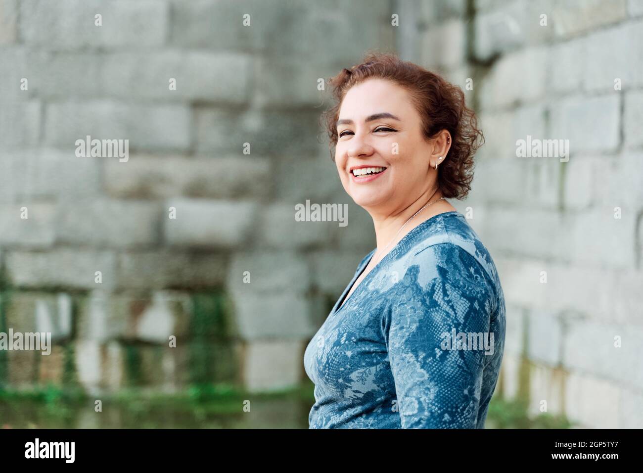 Riant femme mûre dans la ville regardant la caméra. Femme REDHEAD avec cheveux courts, piercing et dents parfaites. Concept de style de vie Banque D'Images