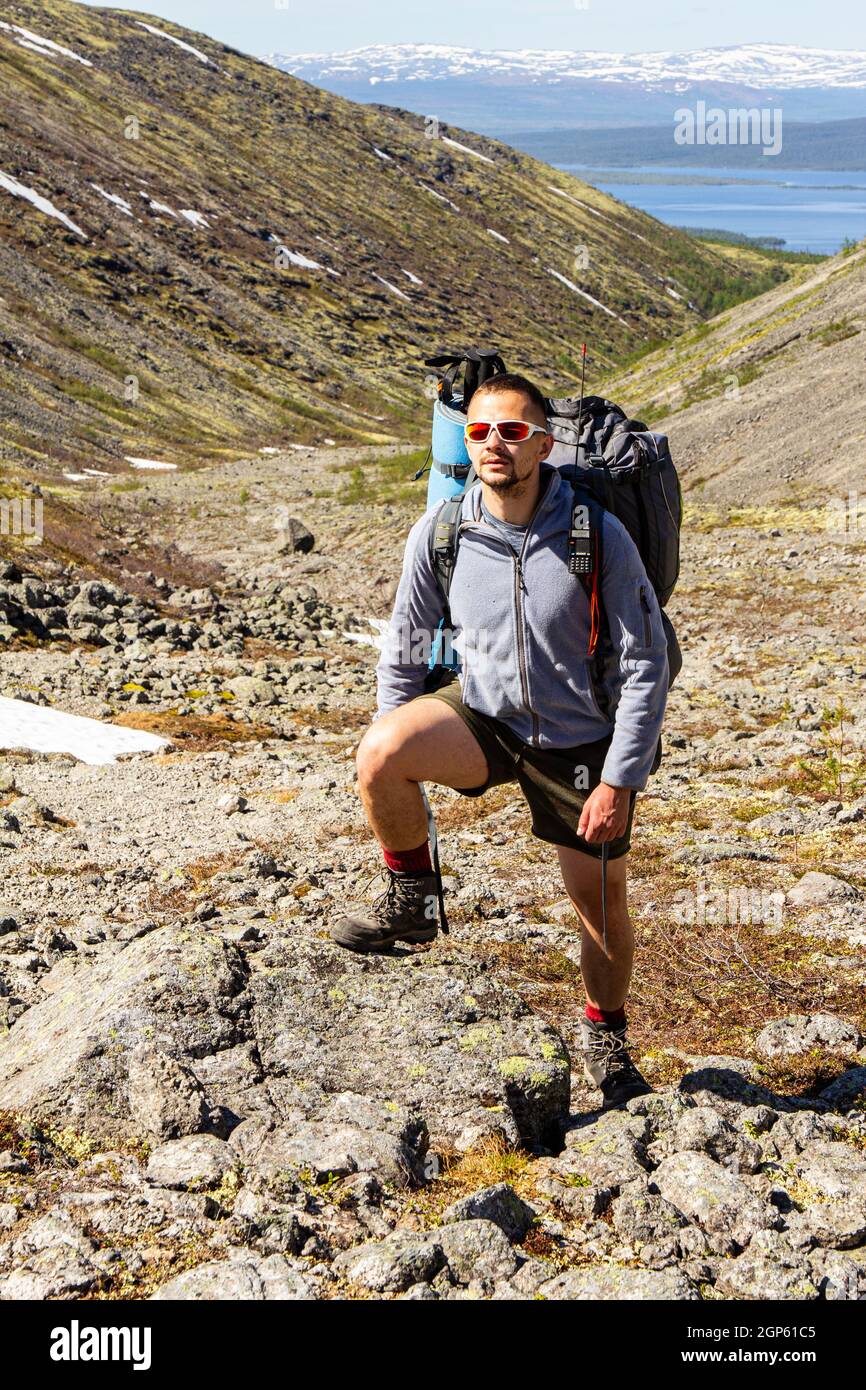 Un touriste européen en vêtements de sport avec de grands sacs à dos et des bâtons de randonnée monte sur une criée de pierre jusqu'au sommet des montagnes de Khibiny. Les randonneurs de groupe font Banque D'Images