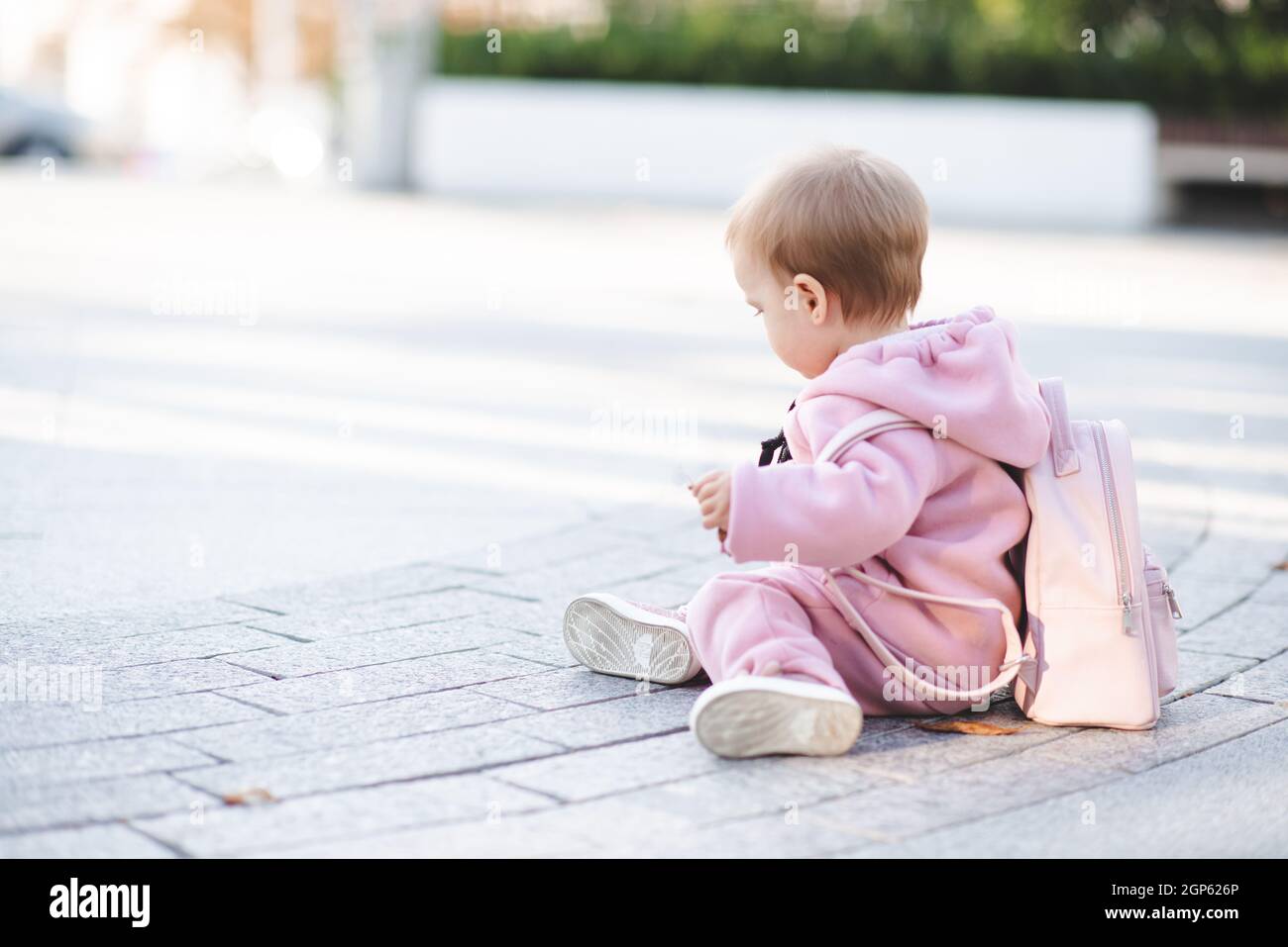 Drôle bébé fille 1 an porter élégant costume de sport rose et sac à dos  assis sur la route dans la rue sur fond urbain. Joli petit enfant avec c.  Tendance Photo