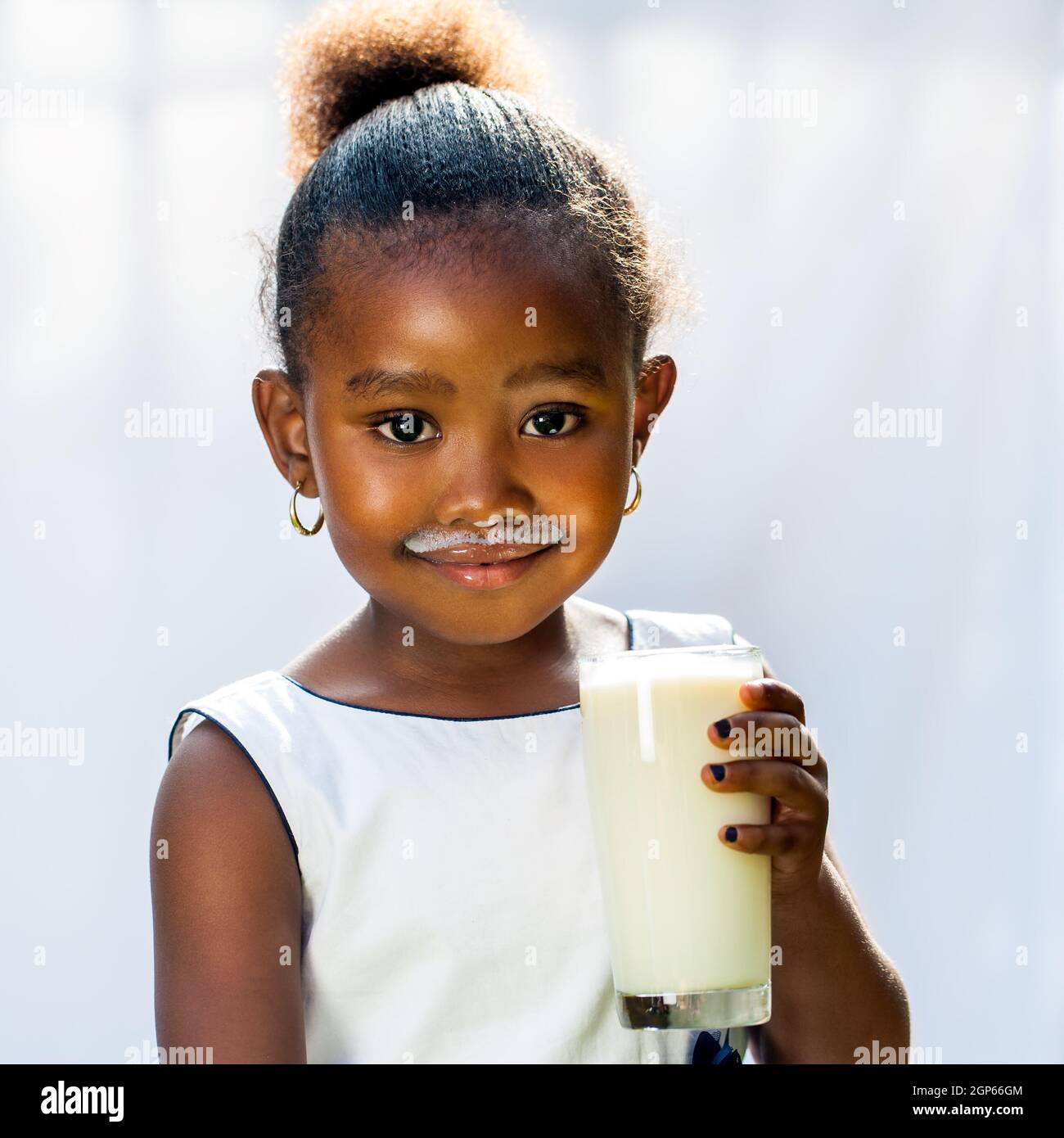 Gros plan portrait d'adorable petite fille africaine buvant un verre de lait.isolé contre fond clair. Banque D'Images