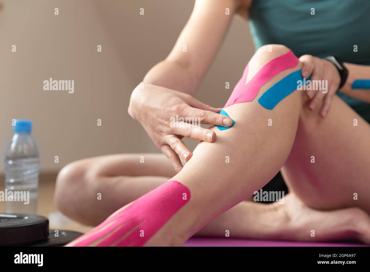 Jeunes femmes en forme appliquant du ruban de kinésiologie élastique sur  son genou. Traitement musculaire, sport de réadaptation et physiothérapie.  Entraînement à la maison Photo Stock - Alamy