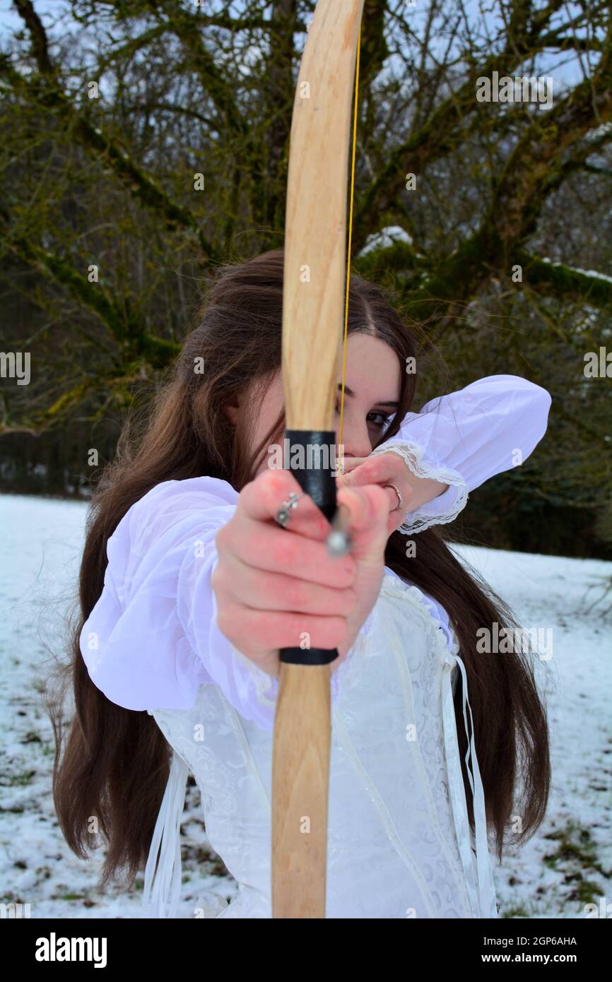 Jeune femme de la façade se tient avec un arc et une flèche dans la neige en face d'une forêt, vise vers l'avant, la main et la tête de flèche hors de foyer Banque D'Images