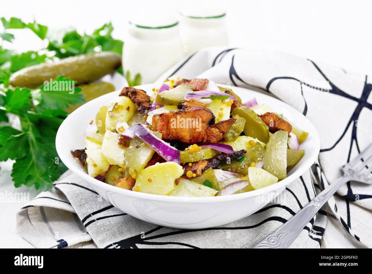 Salade de pommes de terre bouillies, bacon frit, oignons rouges et concombres marinés, assaisonnés de moutarde aux grains, d'épices et d'huile végétale dans une assiette sur une serviette Banque D'Images