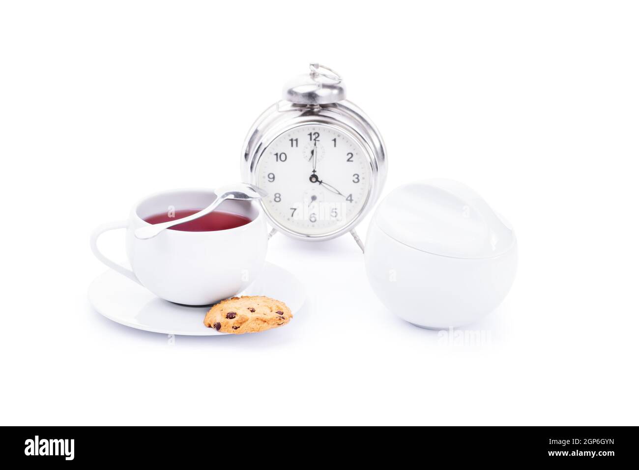 Une tasse de thé blanc avec des biscuits aux pépites de chocolat et un réveil, isolé sur fond blanc. Banque D'Images