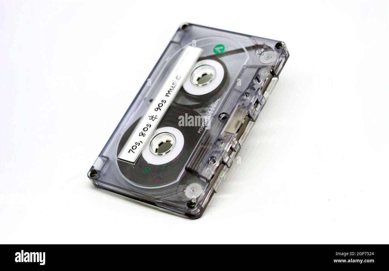 cassette audio transparente avec musique des années 70, 80 et 90 inscrite sur l'étiquette adhésive. Technologie obsolète isolée sur fond blanc. Ana Banque D'Images