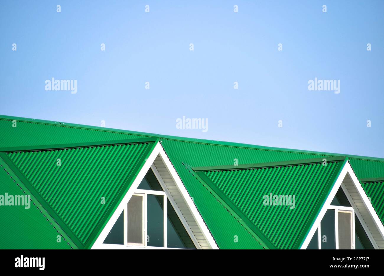 La maison avec des fenêtres en plastique et un toit vert de tôle ondulée.  Toiture de profil métallique de forme ondulée sur la maison avec des  fenêtres en plastique Photo Stock -