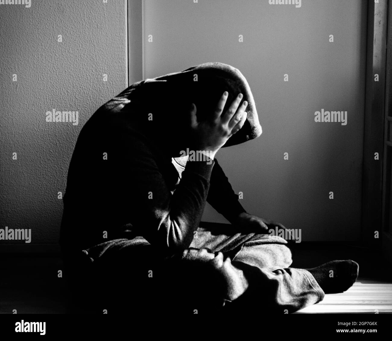 Homme déprimé assis sur le sol à la maison devant un mur de fond blanc Banque D'Images