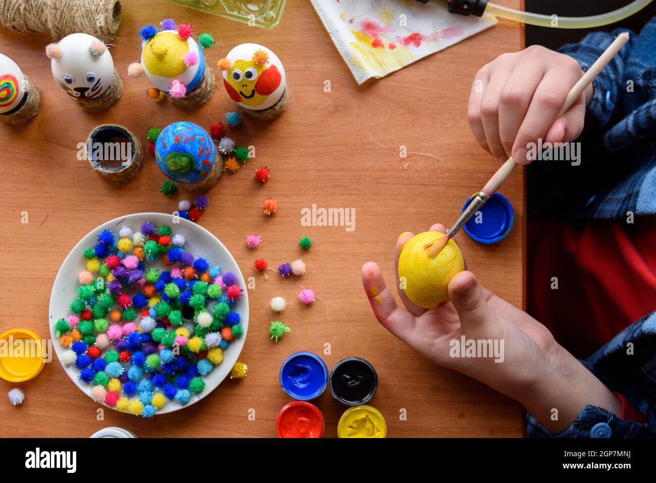 Vue de dessus du bureau et des mains d'un enfant qui peint des œufs de pâques festifs avec des pinceaux Banque D'Images