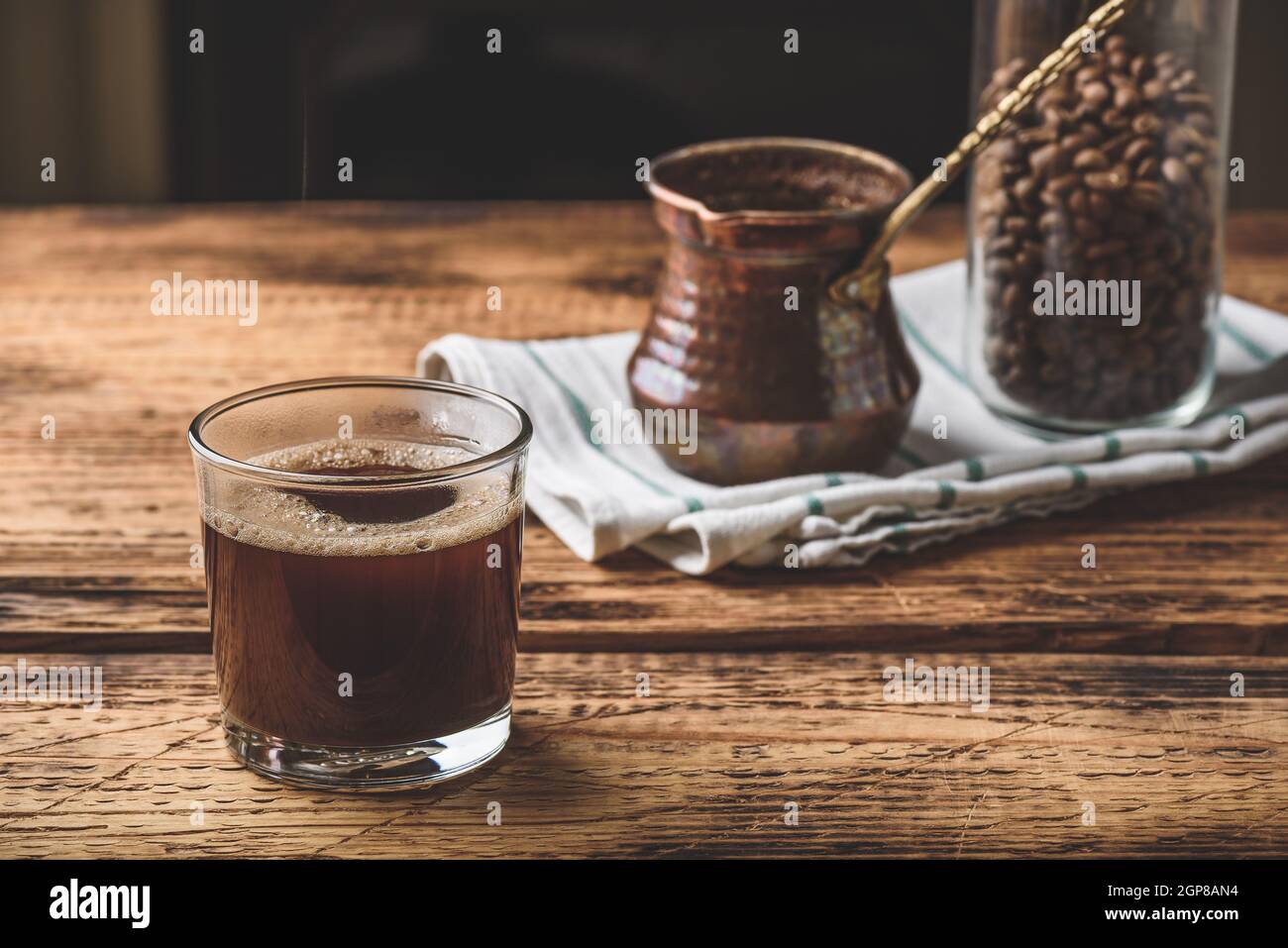 Café turc fraîchement préparé dans un verre à boire. Cezve et pot de grains de café rôtis. Banque D'Images