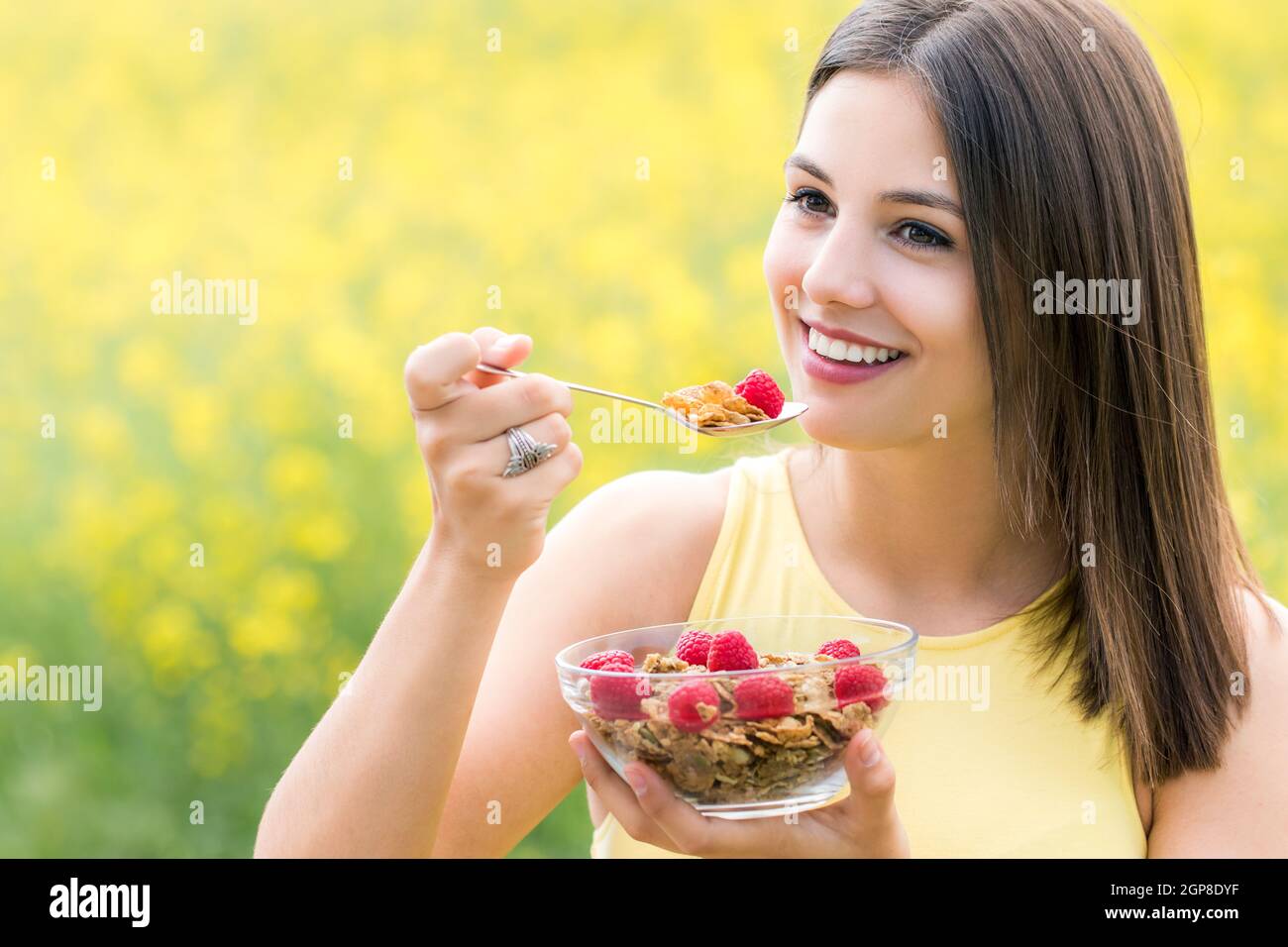 Close up portrait of attractive young woman eating sain croustillant de céréales à grains entiers petit-déjeuner à l'extérieur.Girl holding bowl avec des céréales et la cuillère contre Banque D'Images