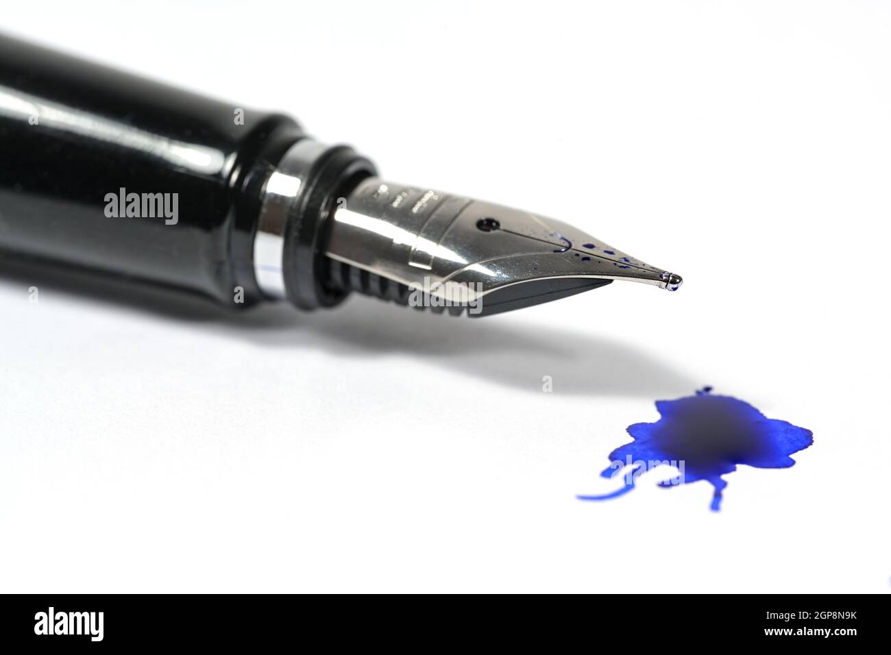 Gros plan d'un stylo plume classique avec une tache d'encre bleue sur fond blanc, espace de copie, mise au point sélectionnée et faible profondeur de champ Banque D'Images