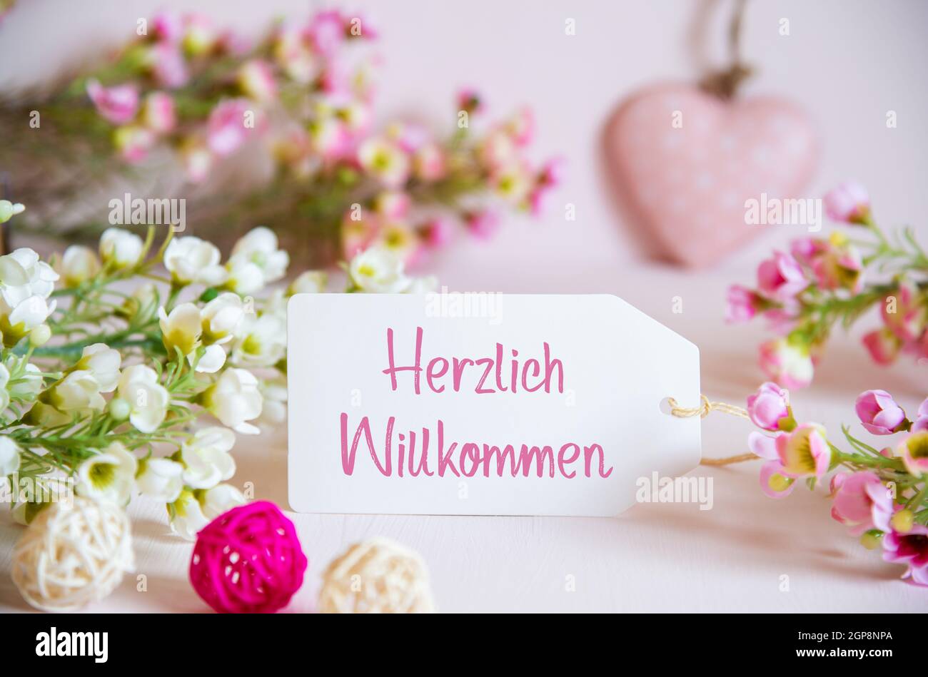 Label avec texte allemand Herzlich Willkommen signifie Bienvenue. Fleurs roses et blanches avec coeur décoratif. Banque D'Images