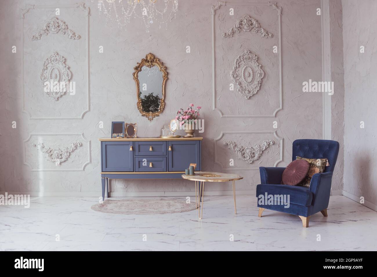 Intérieur luxueux avec commode et fauteuil en velours de style classique, sol en marbre, décoration en stuc sur les murs Banque D'Images